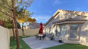 A backyard with artificial grass, a patio table with chairs, and a red umbrella. - One story, 3bedrooms. 15 min from Strip. Quiet & and safe. (Las Vegas)