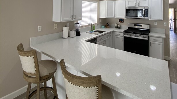 A modern kitchen with white cabinetry, a central island with bar stools, and a stainless steel stove. - One story, 3bedrooms. 15 min from Strip. Quiet & and safe. (Las Vegas)