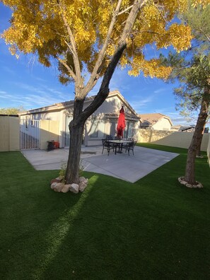 Un jardin avec une terrasse, une table à manger et un parasol rouge.