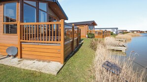 A row of wooden cabins by a calm lake, each with a deck and large windows. - 2 bedroom accommodation in Addlethorpe, near Skegness (Addlethorpe, near Skegness)