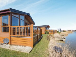 Une rangée de cabanes en bois bordant un lac paisible, chacune dotée d’une terrasse et de grandes fenêtres.