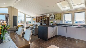A spacious living area with a large dining table, a kitchen with modern appliances, and large windows offering views of the outside. - 2 bedroom accommodation in Addlethorpe, near Skegness (Addlethorpe, near Skegness)
