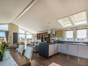A spacious living area with a large dining table, a kitchen with modern appliances, and large windows offering views of the outside. - 2 bedroom accommodation in Addlethorpe, near Skegness (Addlethorpe, near Skegness)