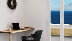 Una habitación con escritorio, ordenador portátil, silla y vista al mar a través de un ventanal.
