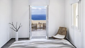 Un dormitorio con una cama grande, vistas a la playa, una silla de mimbre y un jarrón blanco.
