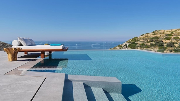 Piscina infinita con terraza de madera y sillas de descanso con vistas al paisaje costero.