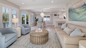 Un salon spacieux avec un grand canapé, une table basse ronde en osier et un coin repas comprenant une table et des chaises blanches.