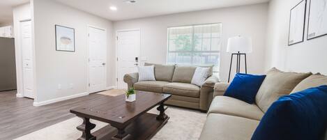 A spacious living room with a beige sofa, a dark wooden coffee table, and a ceiling fan.