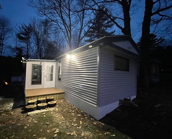 A small, single-story cabin with a front door and a small window, surrounded by trees.