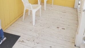 Ein gelbes Zimmer mit zwei weißen Plastikstühlen und einem Fenster mit Jalousien.