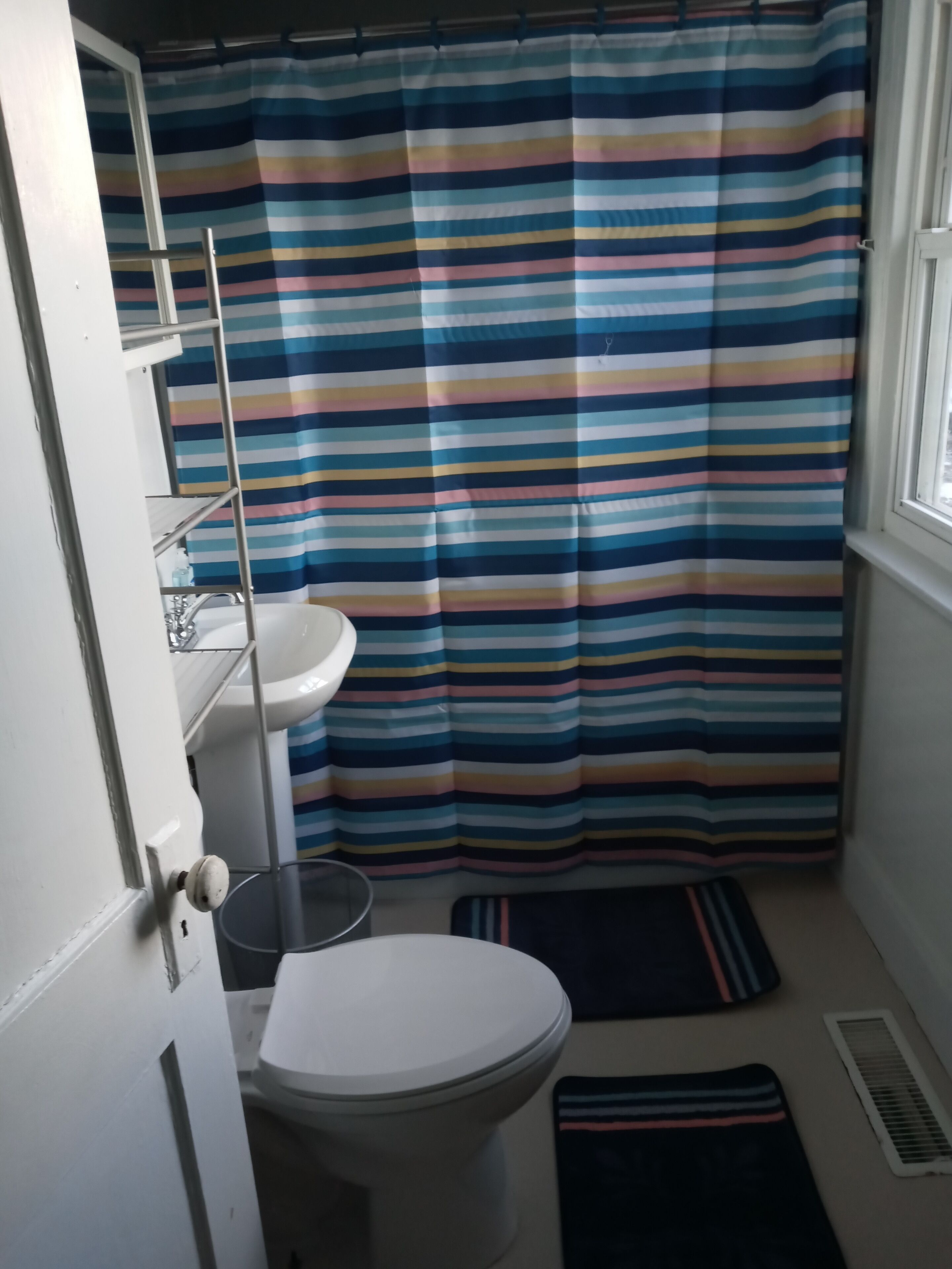 Une petite salle de bain avec un rideau de douche à rayures, un lavabo blanc et des toilettes.