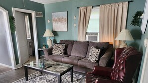 Ein Wohnzimmer mit einem braunen Sofa, einem roten Ledersessel, einem gemusterten Teppich und einem Couchtisch.