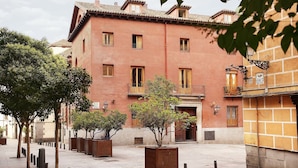 Um edifício de tijolos vermelhos com várias janelas e sacadas, cercado por árvores e floreiras.