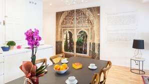 Uma área de refeições com uma mesa posta para dois, um candelabro e um ecrã decorativo com padrões elaborados.