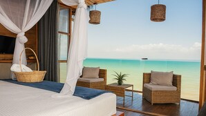 A bedroom with a large bed, a wicker chair, a small table, and a view of the ocean. - Amāra Beach Eco Hotel (Dibulla)