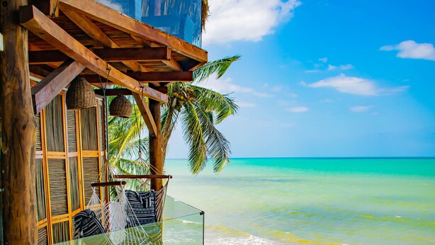 A wooden structure with a glass balcony overlooking turquoise ocean waves. - Amāra Beach Eco Hotel (Dibulla)