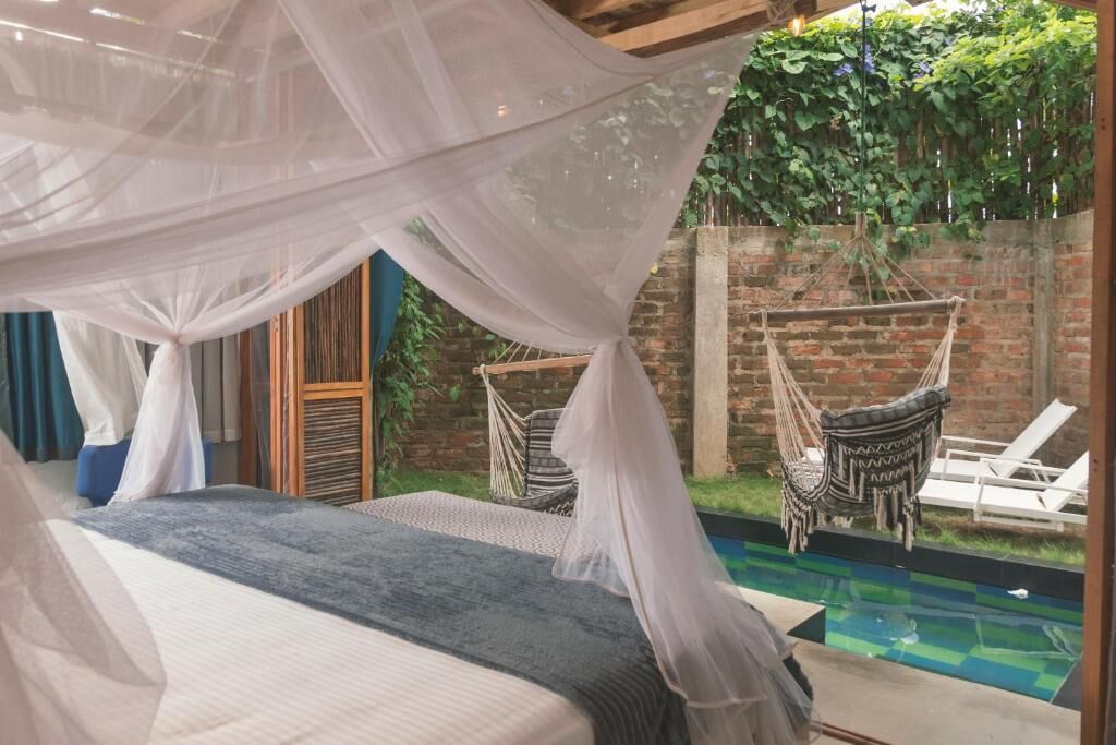 A bedroom with a bed under a canopy, a brick wall, a hanging chair, and a pool.