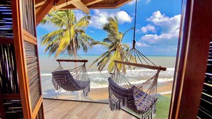 A wooden deck with two hammocks overlooking a beach with palm trees and the ocean. - Amāra Beach Eco Hotel (Dibulla)