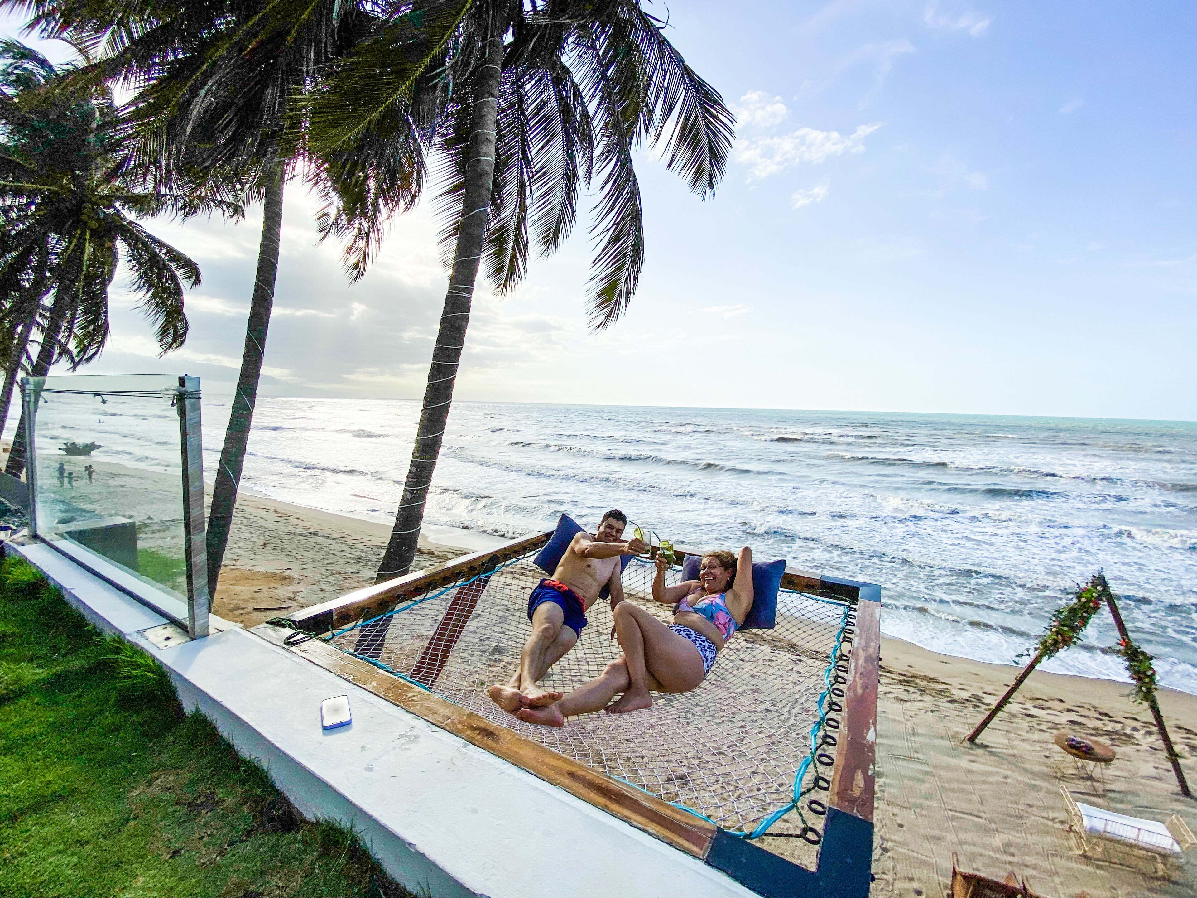 A hammock bed with a view of the ocean and palm trees.