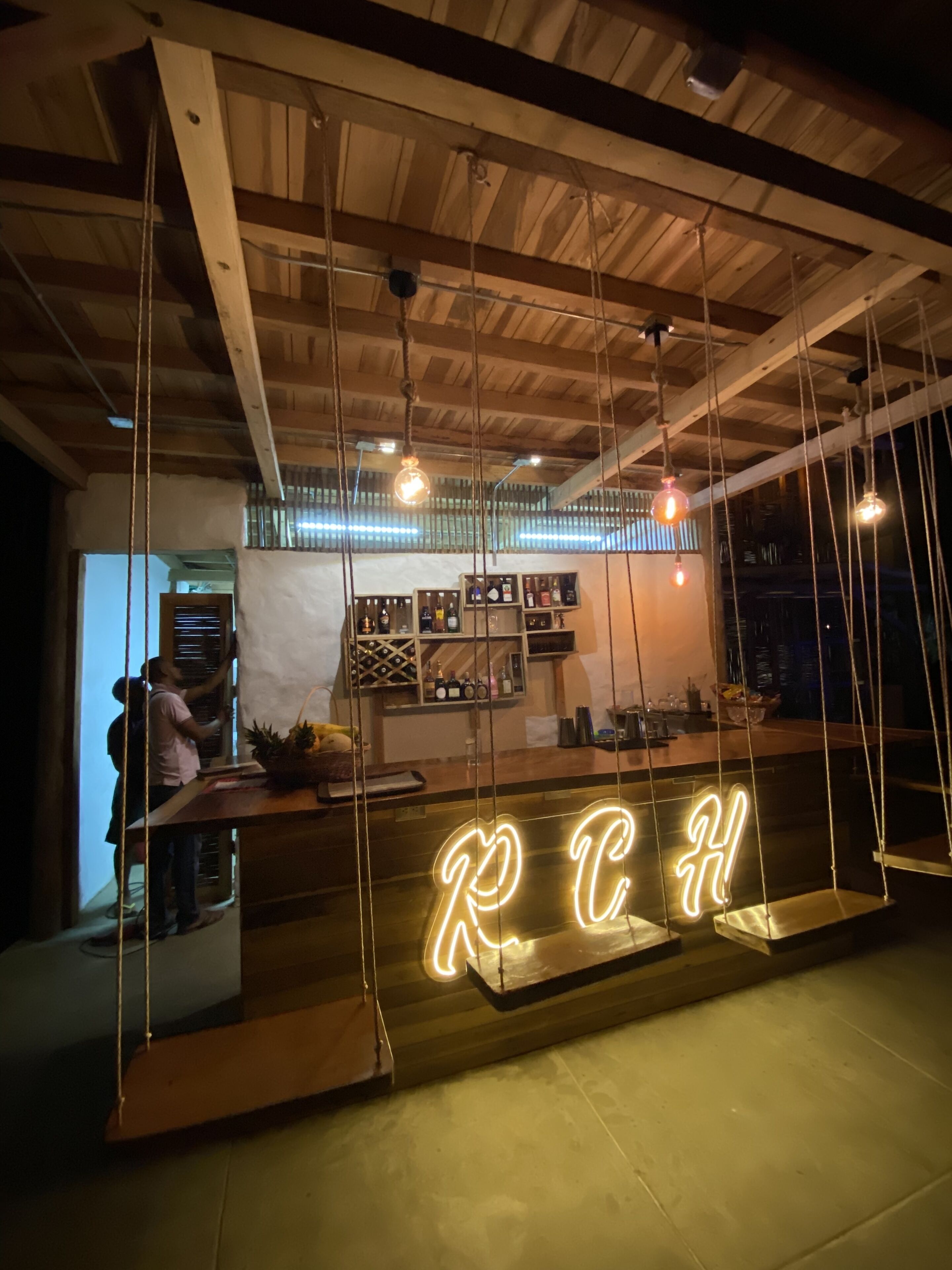 A bar area with a neon sign reading "RCH" and wooden ceiling beams.