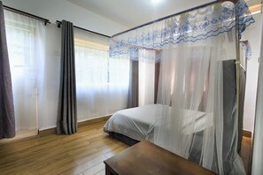 Une chambre à coucher avec un lit, un plancher en bois, un banc et une fenêtre avec des rideaux.