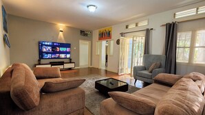 A living room with a flat-screen TV, a sofa set, a coffee table, and a door leading to another room.