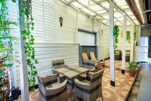 Un patio couvert aménagé avec des meubles en osier, des plantes en pot et une cheminée en pierre.