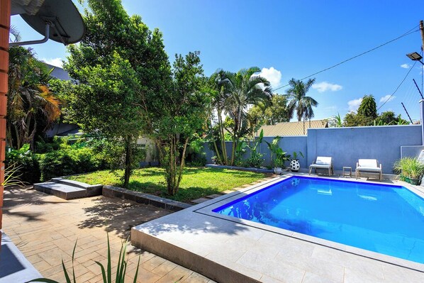 Une piscine dotée d’une terrasse carrelée, entourée de verdure et surplombée par un ciel dégagé.