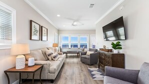 Un salon comprenant un canapé, un fauteuil, une table basse et un téléviseur à écran plat fixé au mur.