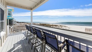 Une terrasse couverte avec vue sur la plage, dotée d’une rambarde et de plusieurs chaises.