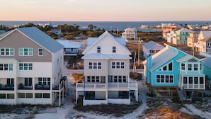 Un quartier résidentiel situé sur la côte, avec des maisons donnant sur la plage, notamment une grande maison blanche dotée d’un balcon et une maison bleue avec une véranda.