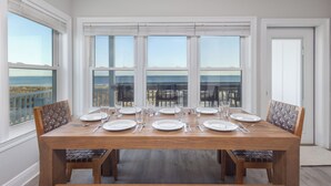 Une salle à manger avec une grande table dressée pour six personnes, de grandes fenêtres donnant sur l’océan et un balcon.