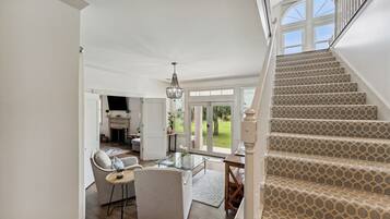 Amplia sala de estar con una escalera que lleva a un balcón, una mesa de centro de vidrio y vistas al exterior.