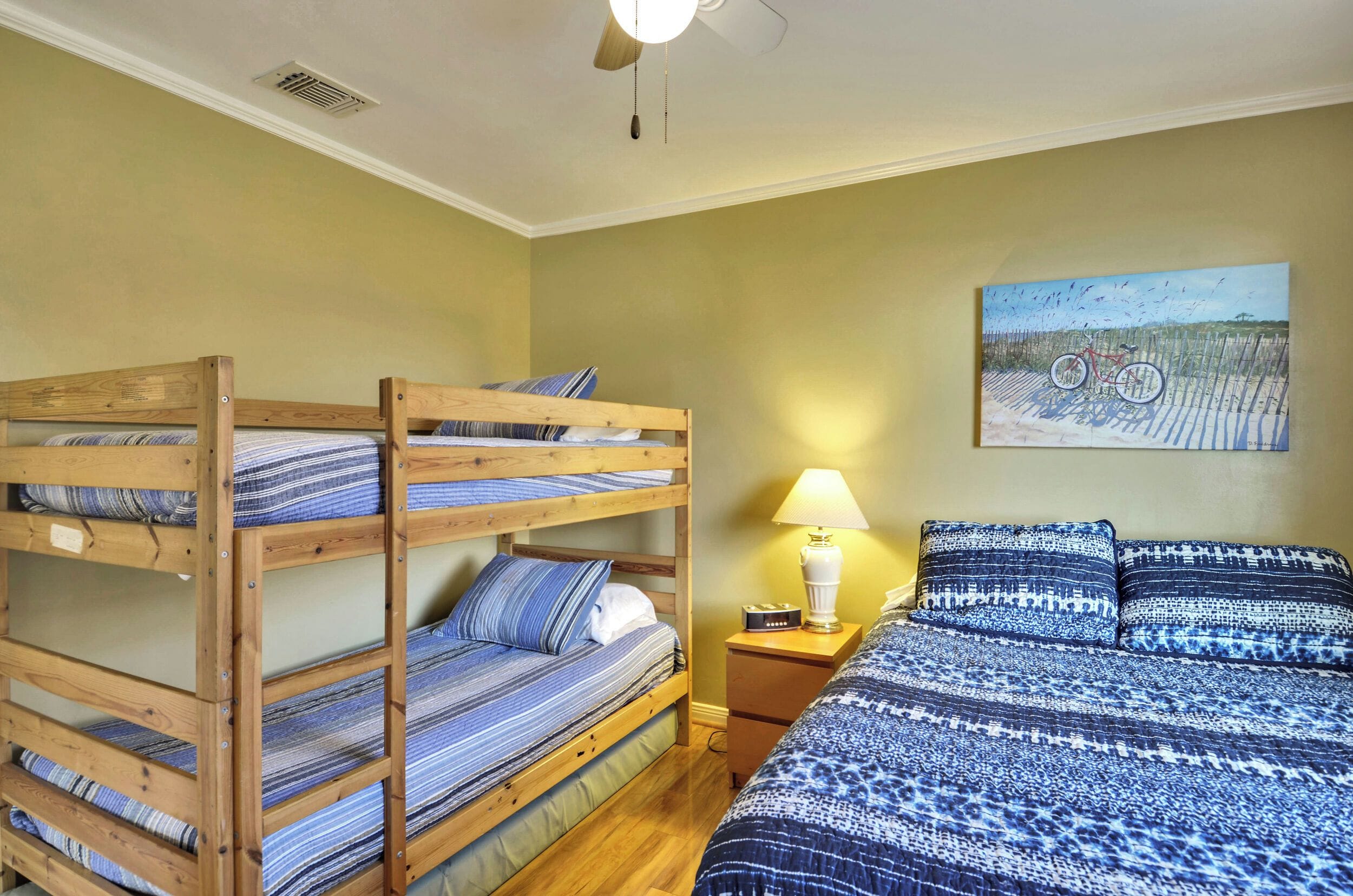 A bunk bed room with a wooden headboard, a nightstand with a lamp, and a painting on the wall.