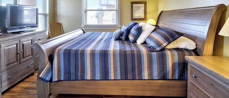 A bedroom with a bed, a TV, a desk, and a window.