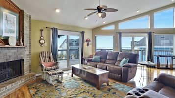 A spacious living room with a fireplace, a ceiling fan, a large window, and a balcony with a view.