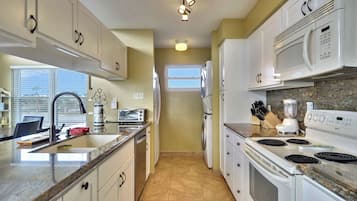 A modern kitchen with white cabinets, a granite countertop, a built-in oven, a microwave, and a window.