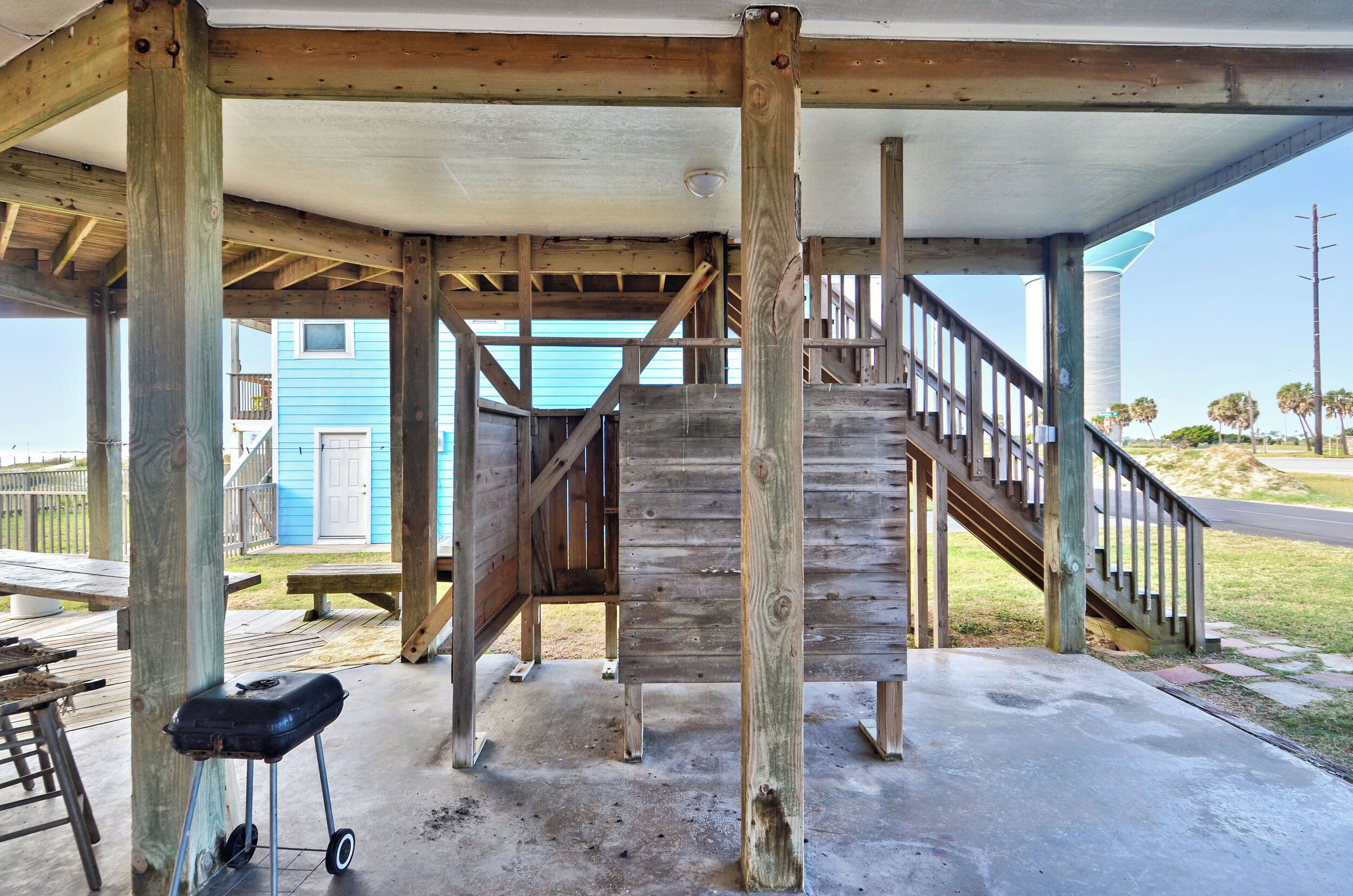 A wooden structure with a staircase, a barbecue grill, and a concrete floor.