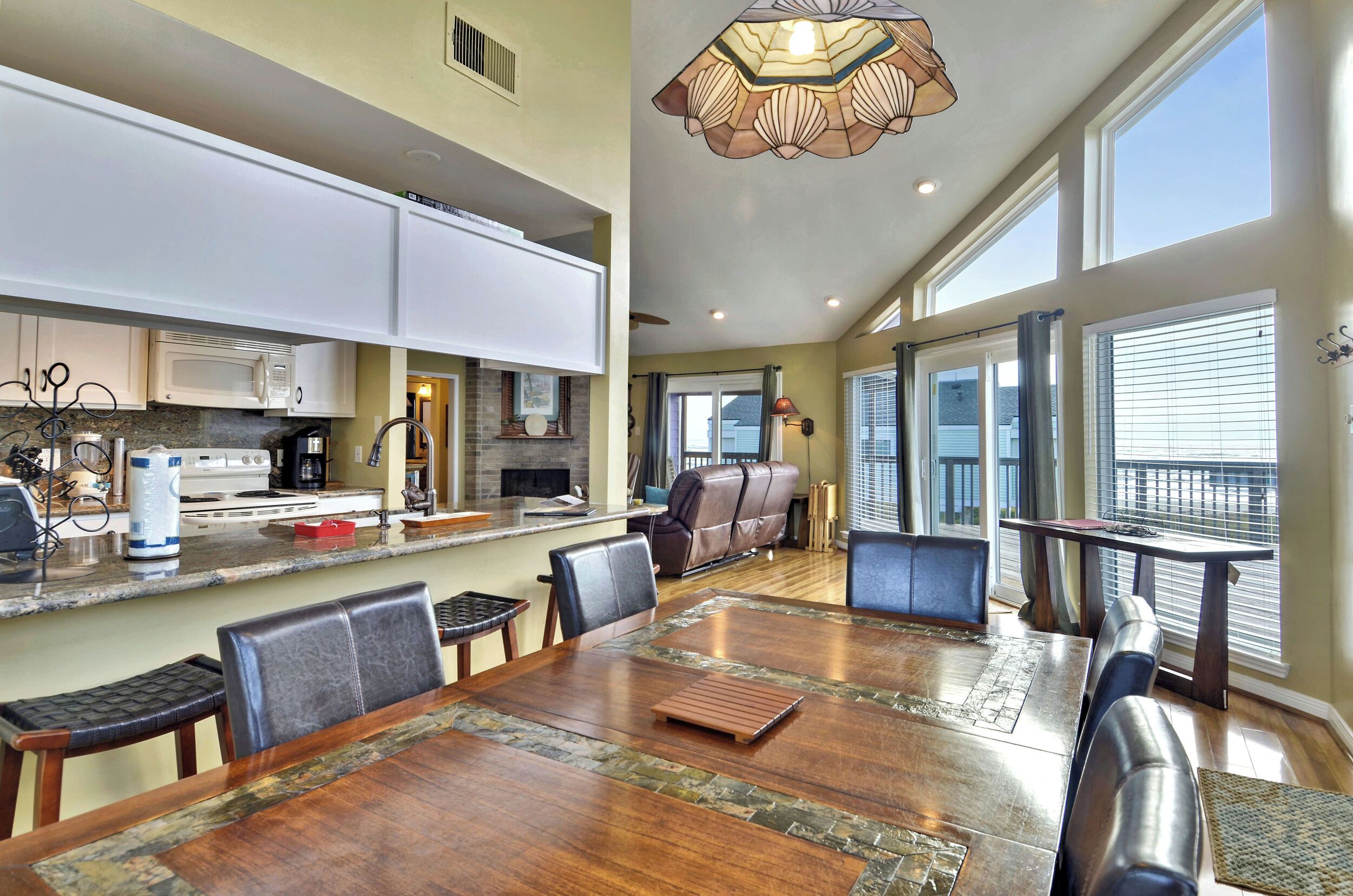 A spacious kitchen with white cabinets, a dining area with a large wooden table, and a view of the outdoors through large windows.
