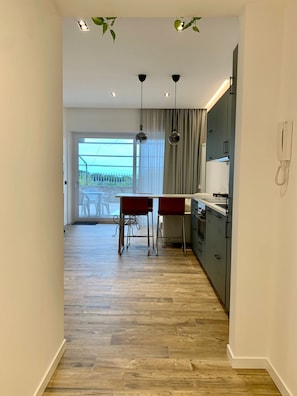 Cocina moderna con comedor, suelo de madera e iluminación colgante.