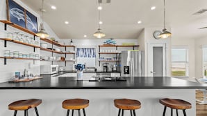A modern kitchen with a central island, bar stools, and a view of the living area. - A Time to Lime by Ryson Vacation Rentals (Galveston)