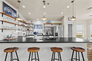 A modern kitchen with a central island, bar stools, and a view of the living area. - A Time to Lime by Ryson Vacation Rentals (Galveston)