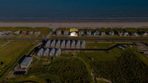 An aerial view of a coastal area with a row of houses, a beach, and a parking lot. - A Time to Lime by Ryson Vacation Rentals (Galveston)