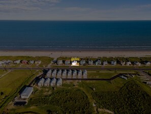 An aerial view of a coastal area with a row of houses, a beach, and a parking lot. - A Time to Lime by Ryson Vacation Rentals (Galveston)