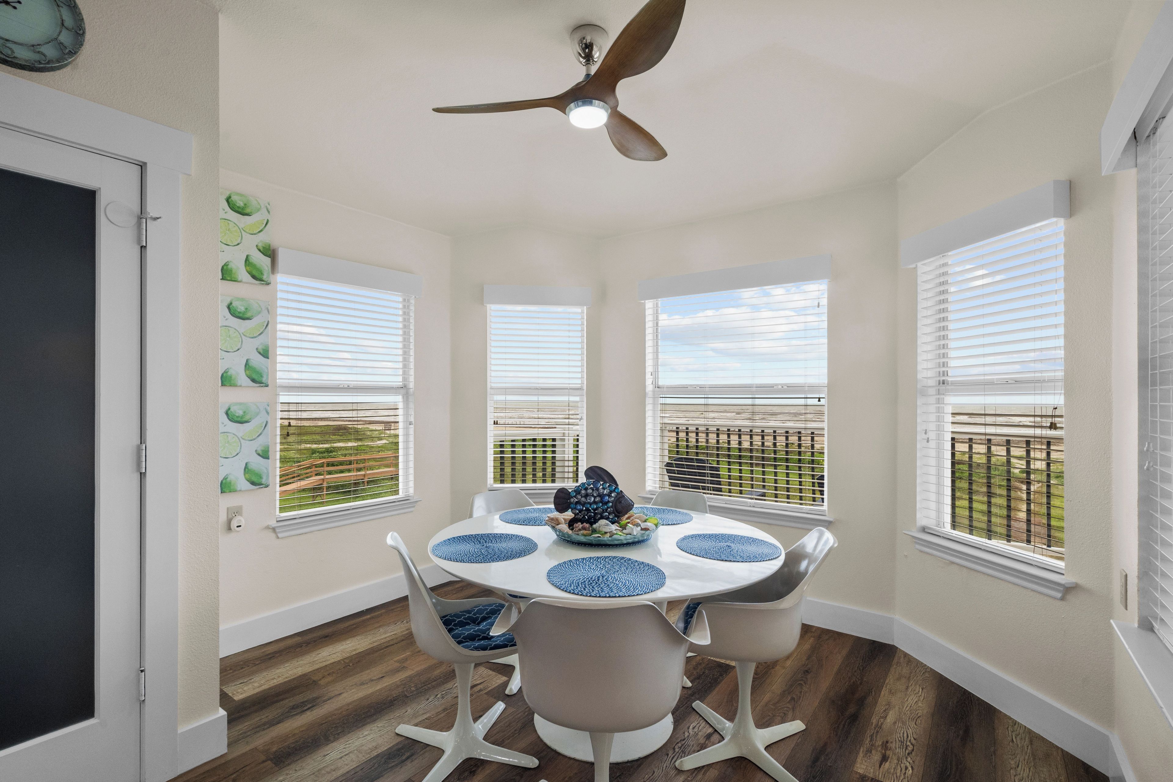 A dining area with a round table, white chairs, and a ceiling fan.