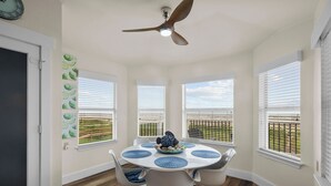 A dining area with a round table, white chairs, and a ceiling fan. - A Time to Lime by Ryson Vacation Rentals (Galveston)