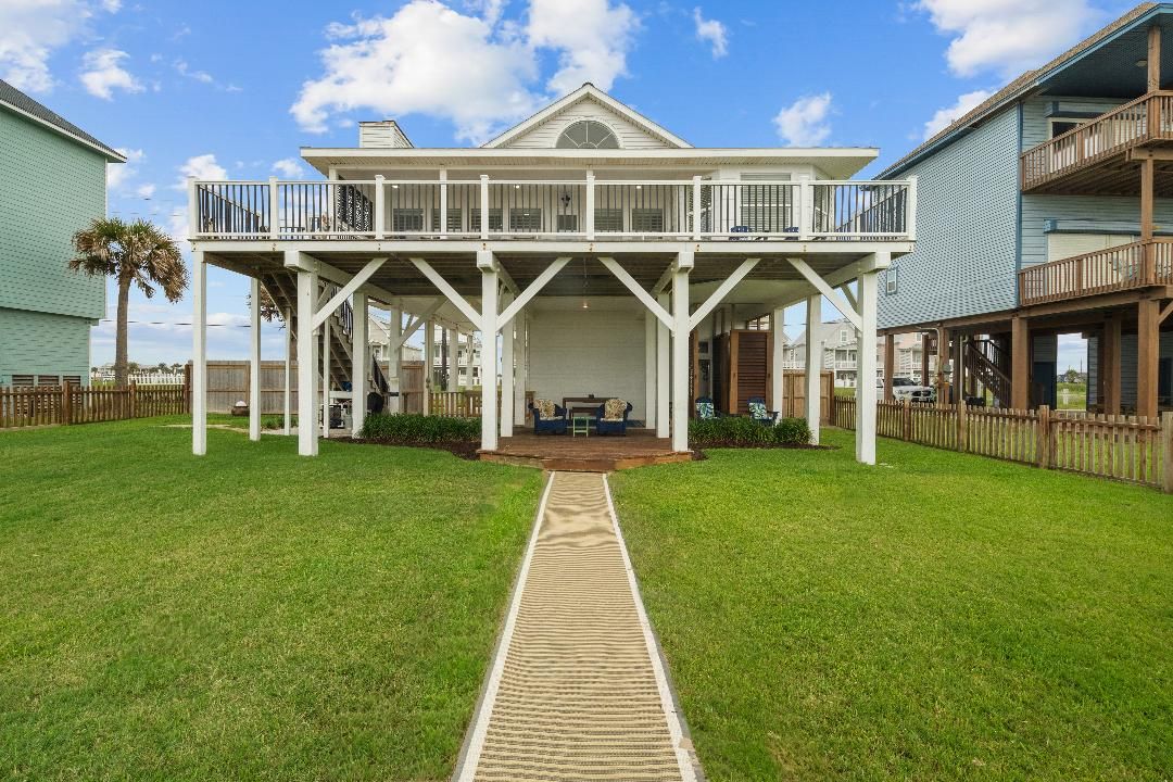 Une maison située en bord de mer, dotée d’un porche abrité, d’une terrasse en bois et d’un chemin menant à l’entrée.