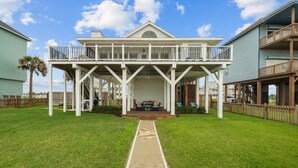 A beachfront house with a covered porch, a wooden deck, and a pathway leading to the entrance. - A Time to Lime by Ryson Vacation Rentals (Galveston)