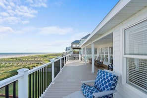 A covered deck with a view of the beach, outdoor furniture, and a railing.