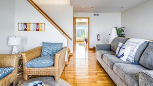 Una sala de estar con mobiliario de mimbre, un sofá gris y una escalera que lleva a otra habitación.